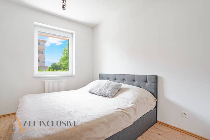 A bedroom in a 2-room apartment with a bed and a view of greenery through the window.