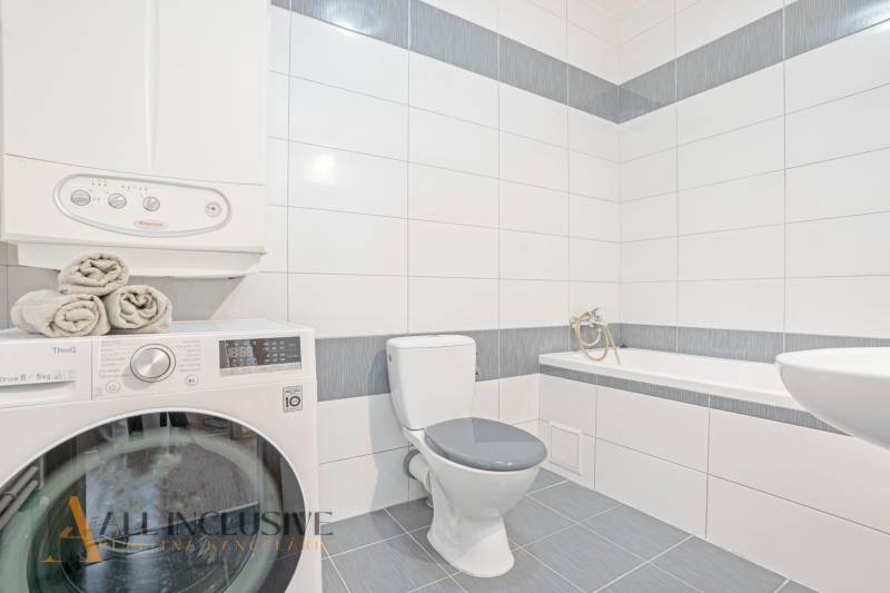 Bathroom in a 2-room apartment with a shower, washing machine, and toilet, bright tiles.