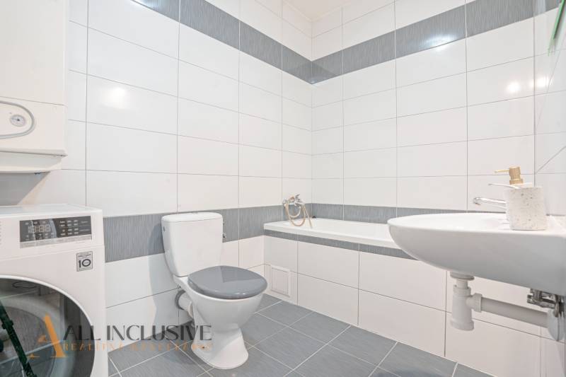 Bathroom with a bathtub, washing machine, and toilet in a 2-room apartment.
