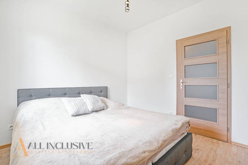 A bedroom in a two-room apartment with a bed and wooden doors, white interior.