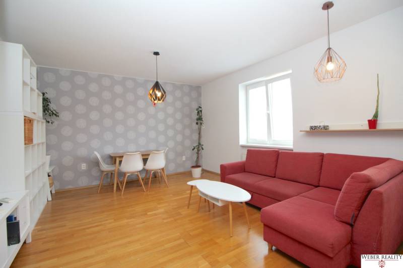 Living room in a two-room apartment with a red sofa, dining table, and white shelf.