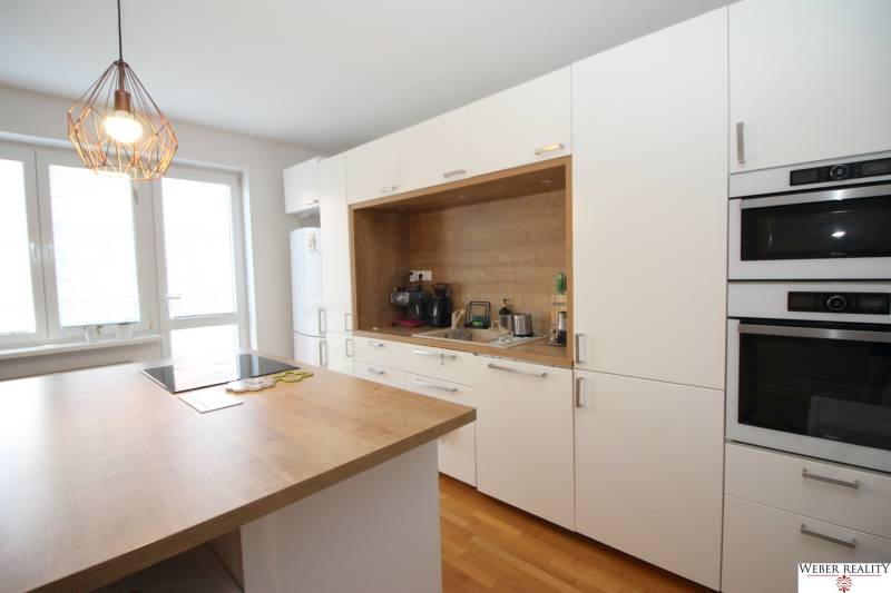 A kitchen in a 2-room apartment with built-in appliances, white cabinets, and wooden flooring.