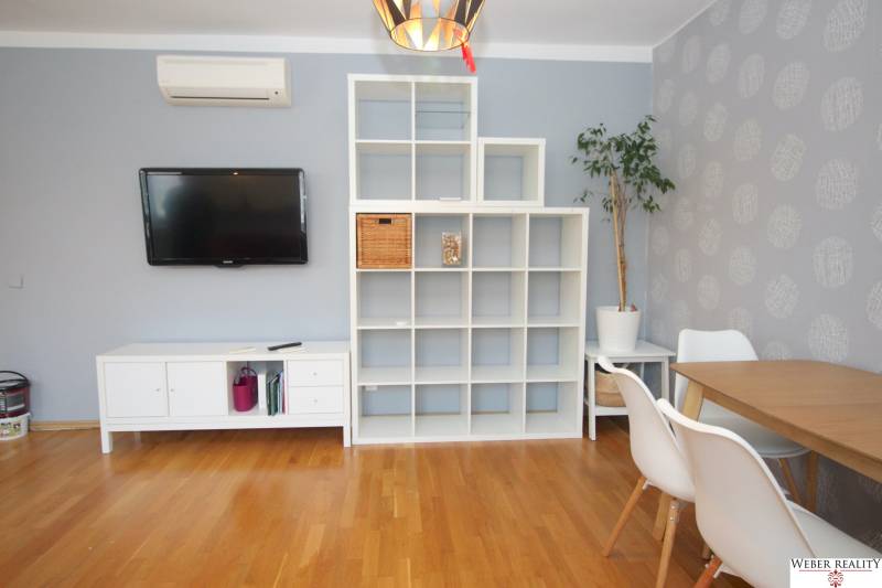 A bright living room in a two-room apartment with a television and a shelving unit.
