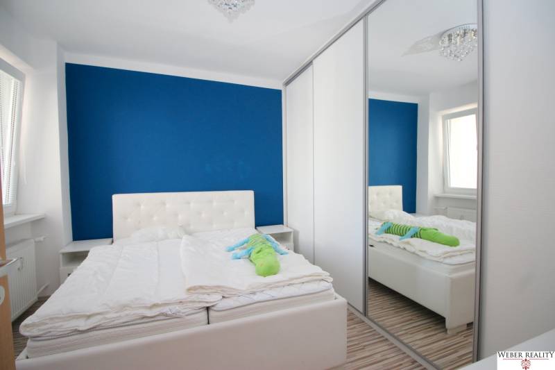 A bedroom in a 2-room apartment with a white bed and a large mirrored wardrobe.