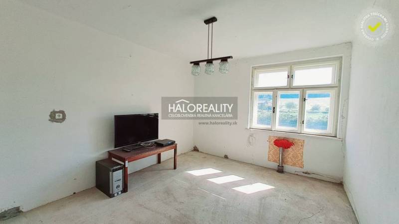 A room in a family house with a window, a table, a television, and a computer.