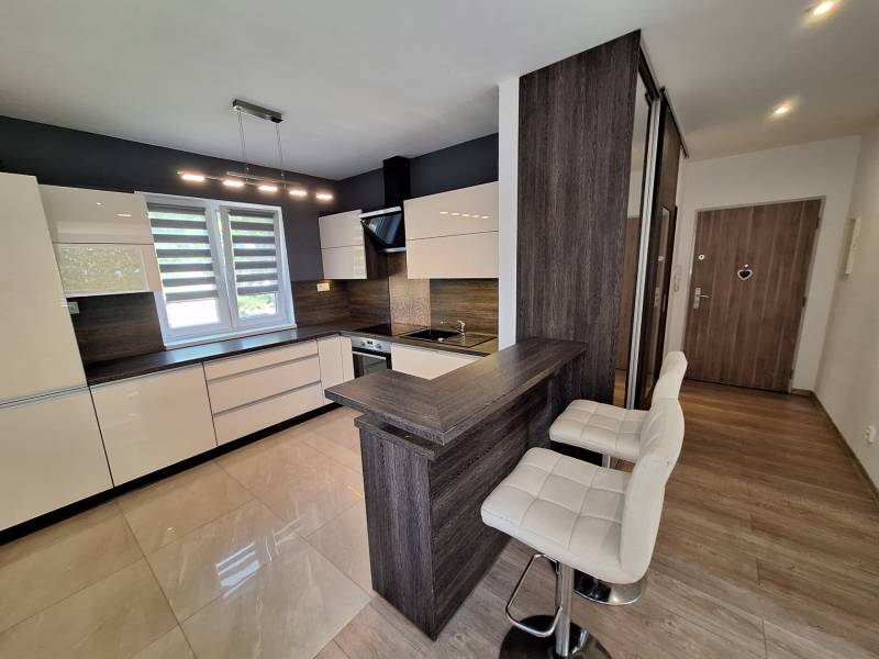 A kitchen in a 4-room apartment with white cabinets, bright lighting, and a bar counter.
