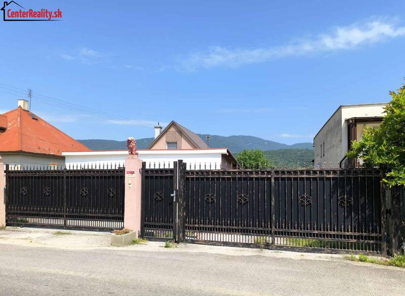 A family house in Nitrica with a large wrought-iron gate and a beautiful mountain backdrop.