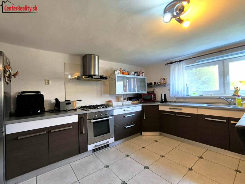 A kitchen in a family house with dark lower cabinets, appliances, tiled floor.