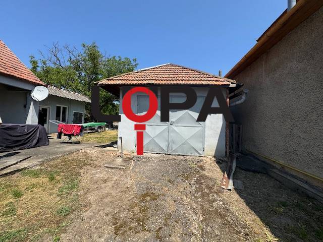 The courtyard of a family house in Mužla with a garage, grass, and a satellite on the roof.