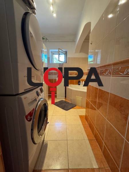 A bathroom in a family house with a washing machine, dryer, and bathtub, tiled with colorful tiles.