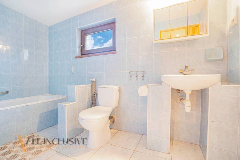 A bathroom in a family house with a bathtub, toilet, and sink. Light blue tiles.