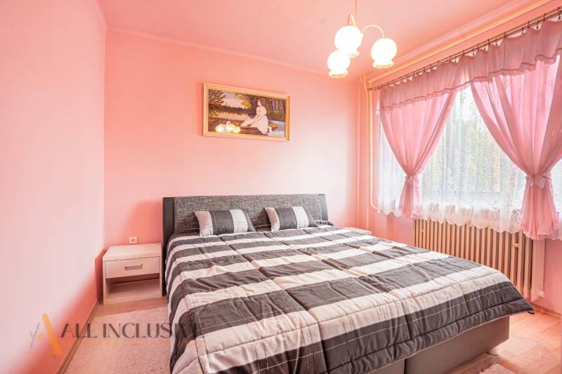 A bedroom with pink walls and curtains, a double bed, a painting, and a nightstand.