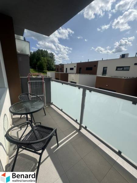 The balcony of a 2-room apartment in Stará Ľubovňa with furniture, a view of modern buildings and greenery.