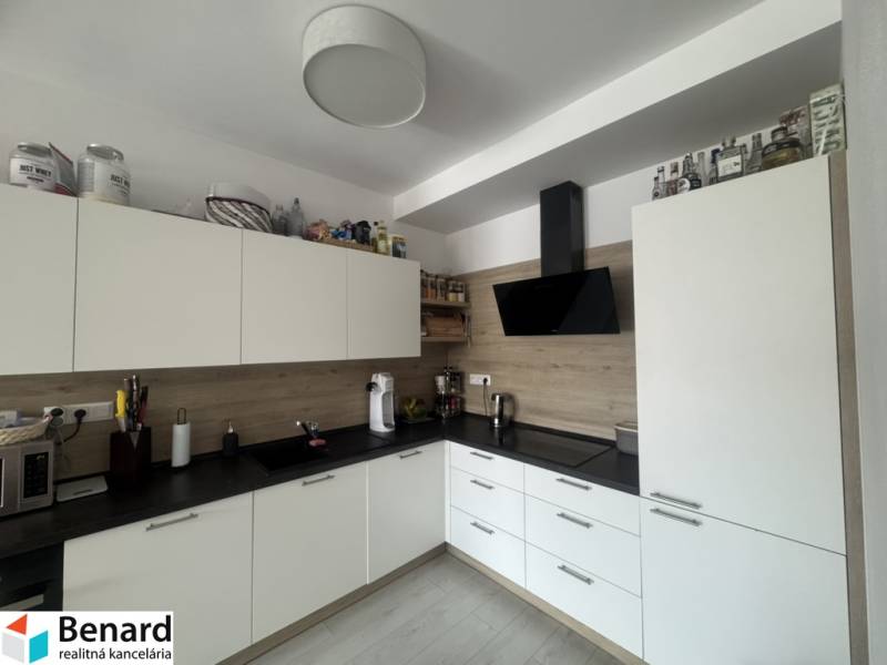The kitchen in a 2-room apartment with white cabinets and a black extractor hood.