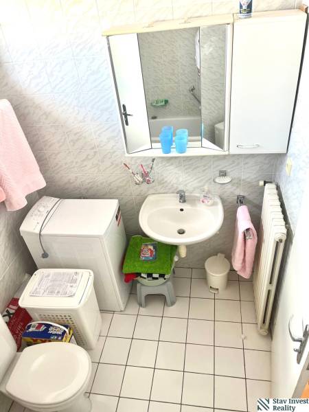 A bathroom with a sink, washing machine, toilet, and white tiles in commercial premises.