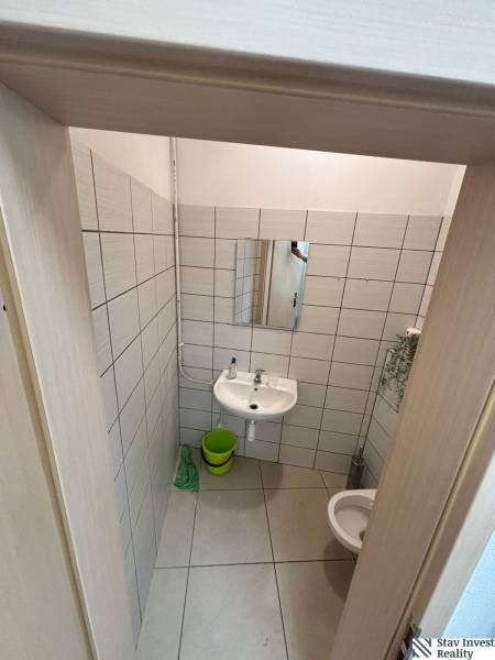 A restroom with a mirror, sink, and green bucket in commercial premises.