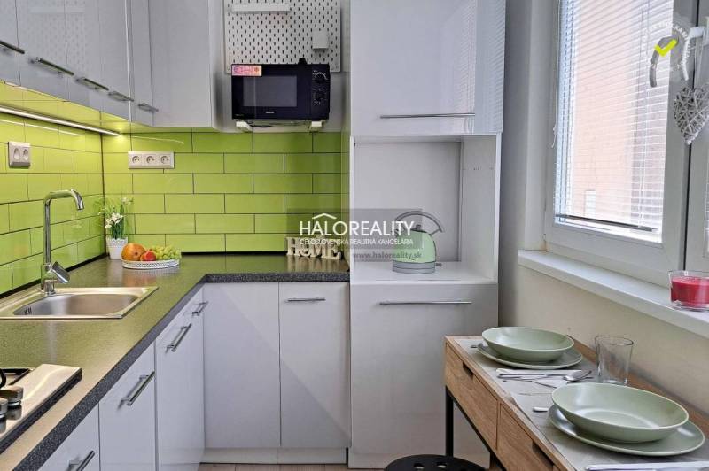 A kitchen in a studio apartment with white cabinets and green tiles.