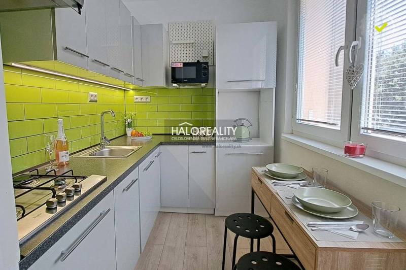A kitchen in a studio apartment with green tiles and a dining table for two people.