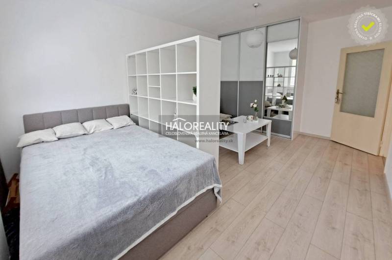 A bright room with a bed, a dividing shelf, and a table in a studio apartment.