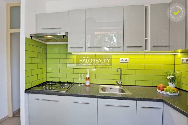 A kitchen in a studio apartment with a gas stove, green tiles, and a stainless steel sink.