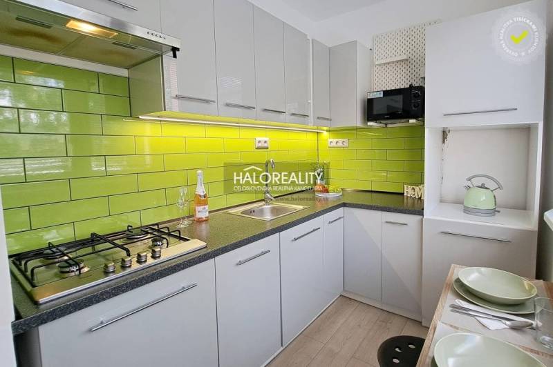 A kitchen unit with green tiles, a hob, and dishes in a studio apartment.