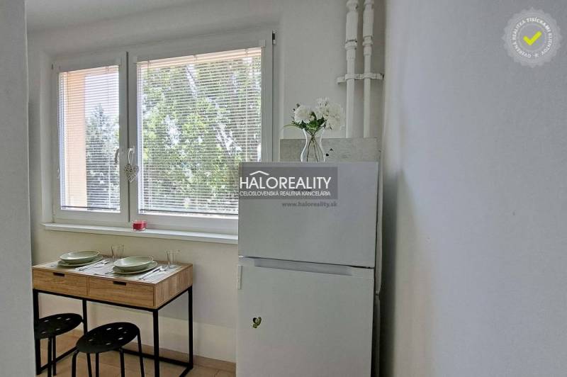 Dining area in a studio apartment with a refrigerator and a table by the window.
