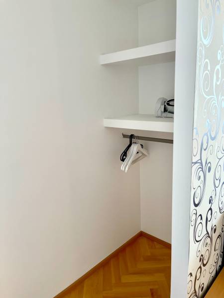 A wardrobe in a 2-room apartment with wooden flooring, shelves, and hangers.