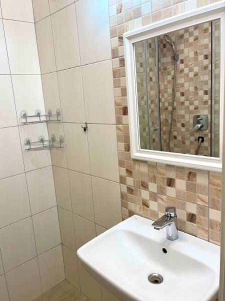 A bathroom in a 2-room apartment with a sink, mirror, and tiles in neutral tones.