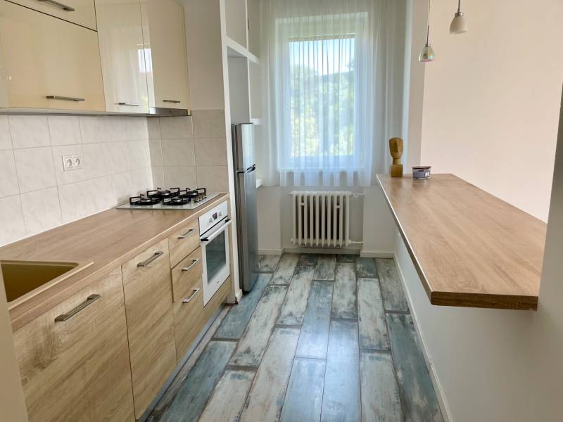 A kitchen in a 2-room apartment with built-in appliances, a wooden countertop, and a light floor.