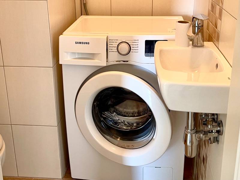 Samsung washing machine next to a compact sink in the bathroom of a 2-room apartment.