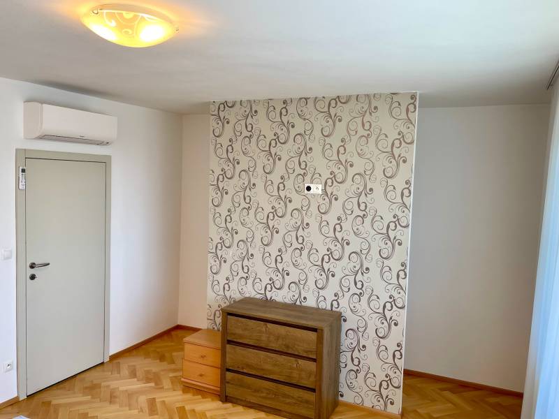 A room in a 2-room apartment with a wooden floor, wallpaper, and a wooden chest of drawers.