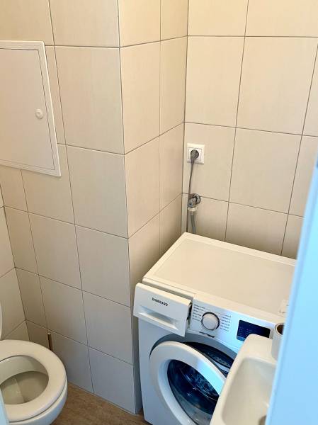 A bathroom with a washing machine in a 2-room apartment, tiled with light tiles.