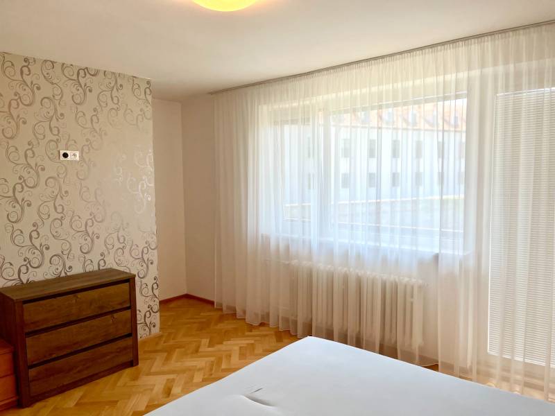 Bedroom in a 2-room apartment with large windows, wooden floor, and a dresser.