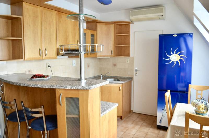 A kitchen in a studio apartment with light wooden furniture, a bar counter, and a blue refrigerator.