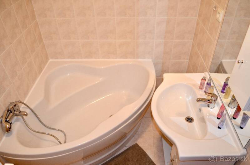 A bathroom with a corner bathtub and a sink in a studio apartment.