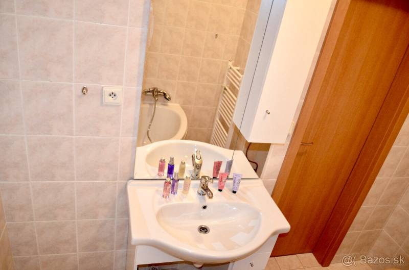 Bathroom in a studio apartment with a sink, bathtub, and mirror, beige tiles.