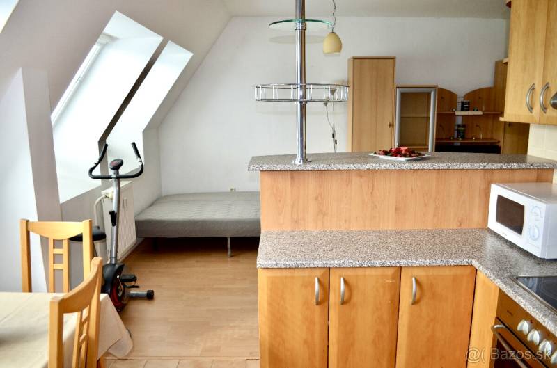 Kitchen corner in a studio apartment with a bed, table, and exercise equipment.