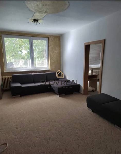 A sofa in the living room of a 3-room apartment with a large window and a carpet.