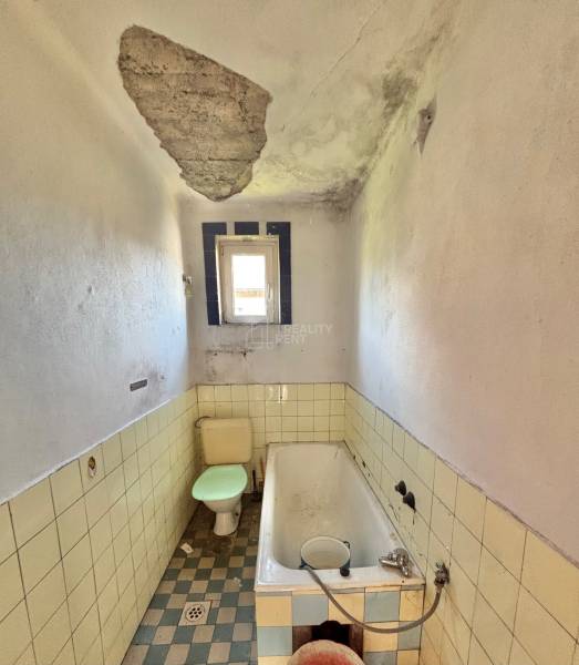 A worn-out bathroom in a family house with a damaged ceiling, bathtub, and toilet.