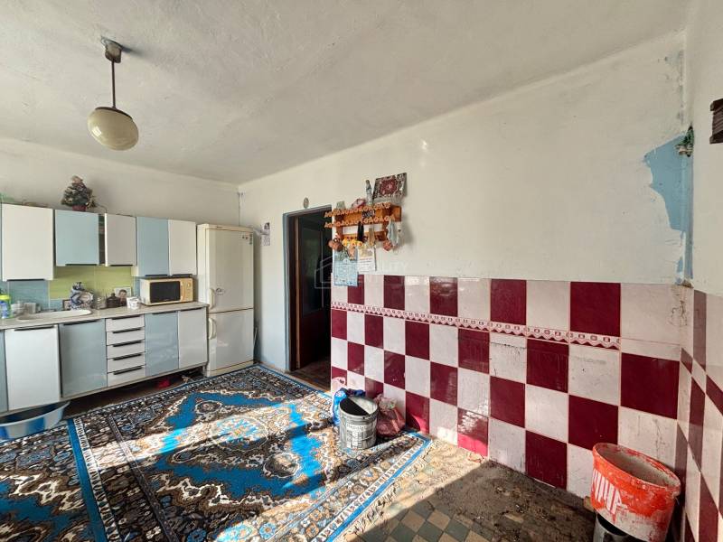 A kitchen in a family house with carpets, white cabinets, and red and white tiles.