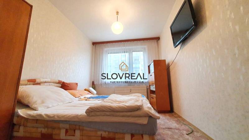 A bedroom in a three-room apartment with a TV on the wall and a bed.