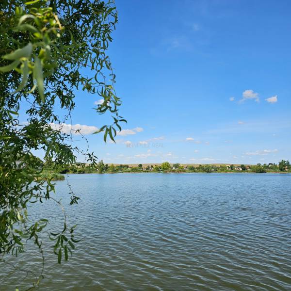 A lake surrounded by greenery under a blue sky in Čaňa, near a cottage.
