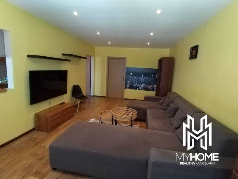 A living room in a three-room apartment with a comfortable sofa and a TV on the wall.
