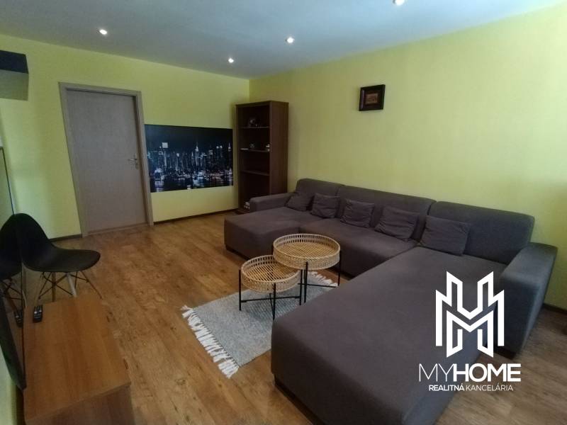 Living room with wooden flooring, gray sofa, chairs, and light yellow walls in a three-room apartment.