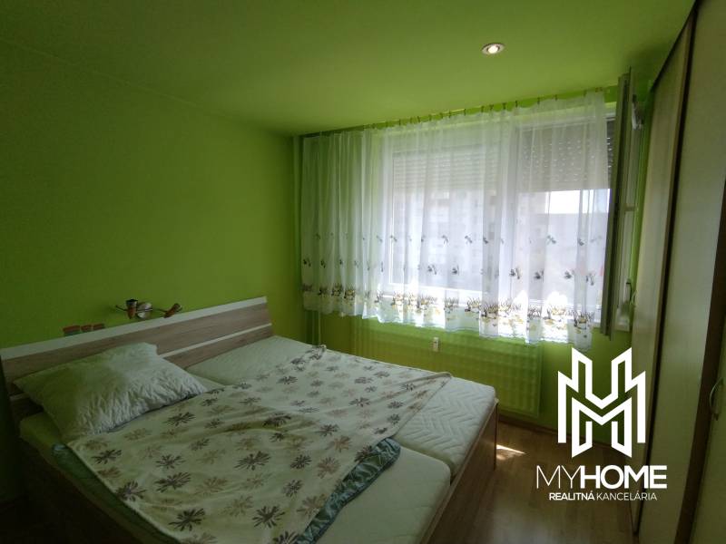 Green bedroom with a double bed and a large window in a three-room apartment.