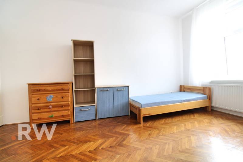 A room in a 3-room apartment with an oak floor, a bed, a wardrobe, and a shelf.