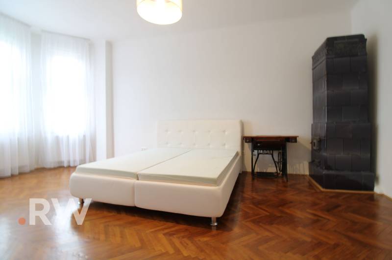 A bright room with an antique tiled stove and a white bed in a 3-room apartment.