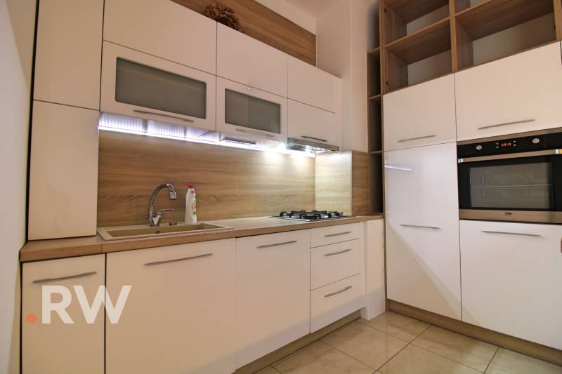 A kitchen in a 3-room apartment with white cabinets and wooden details on the walls.