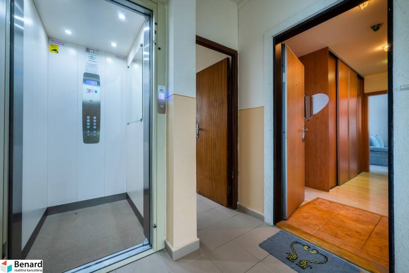 A hallway with an elevator and entrance to a 3-room apartment with wooden doors.