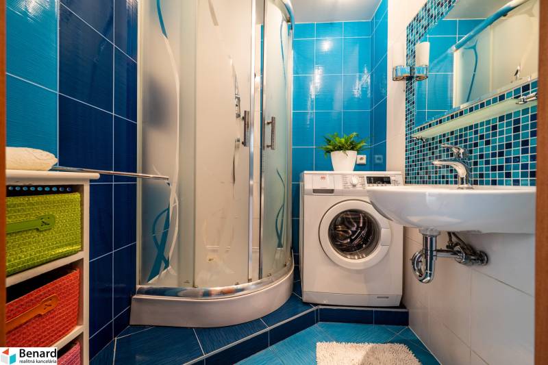 A bathroom in a 3-room apartment with a washing machine, shower corner, and blue tiles.